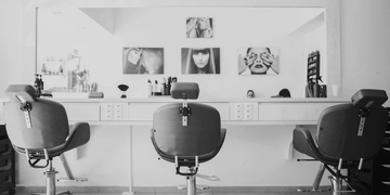 Black and white photo of three salon chairs and mirrors.