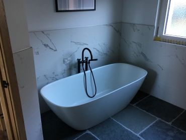 Modern white bathtub with black fixtures in a tiled bathroom.