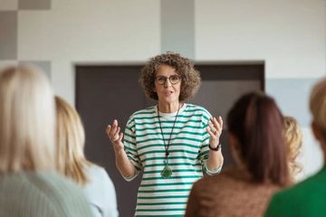 Woman with curly hair speaking to an audience indoors.
