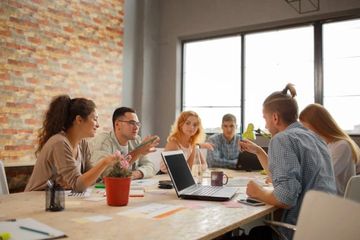 A group discussing ideas around a table with laptops and notes.