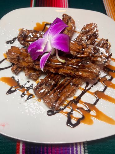 Churros drizzled with chocolate and caramel, garnished with a purple orchid.
