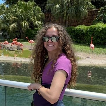A smiling woman with curly hair near a pond with flamingos.