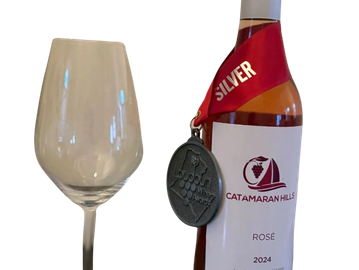 A bottle of award-winning Catamaran Hills Rosé 2024 with a silver medal and empty wine glass.