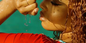 Woman with wet hair holding her fist near her face with water droplets.