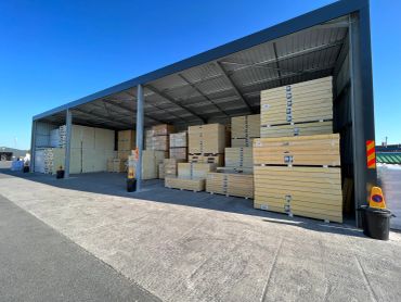 Large outdoor warehouse storing stacks of wooden crates under a metal roof.