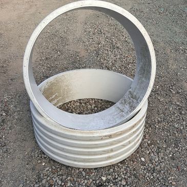 Stacked cylindrical concrete pipes on gravel ground.