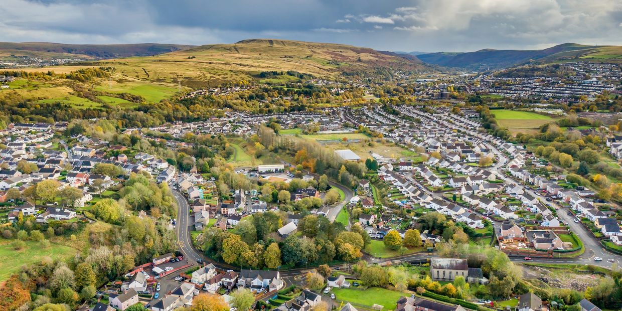 A sprawling suburban town nestled in a green valley with hills in the background.