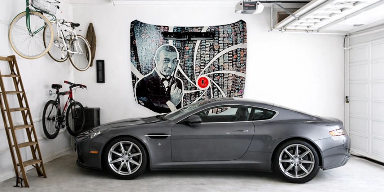 Sleek gray sports car parked in a clean, organized garage with bicycles and a James Bond-themed wall art.
