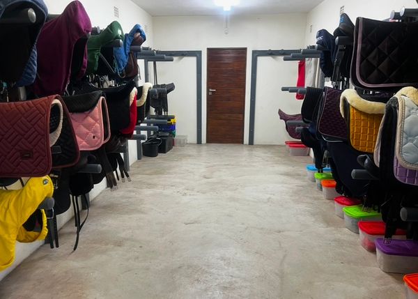 An organized tack room with saddles and equestrian gear neatly hung on racks.