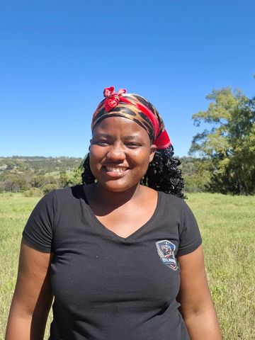 Smiling woman wearing a red and black headscarf outdoors on a sunny day.