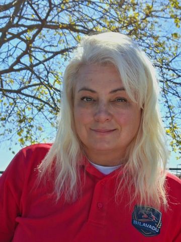 Smiling woman with blonde hair in a red polo shirt outdoors.