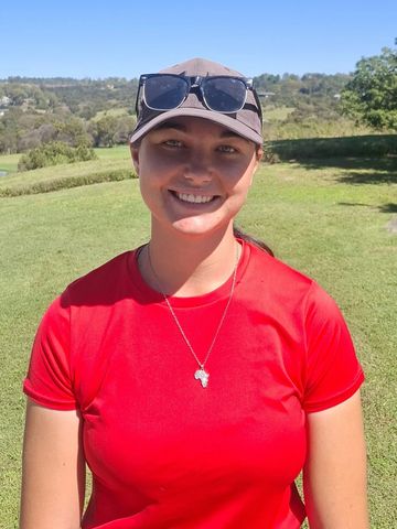Young woman in red shirt smiling outdoors under blue sky.