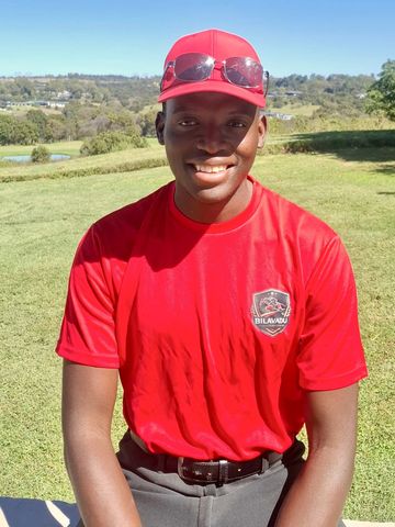 Smiling man in a red shirt and cap outdoors on a sunny day.