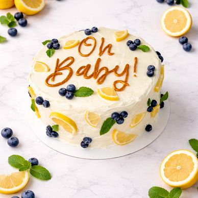 A white frosted cake decorated with lemon slices, blueberries, mint leaves, and "Oh Baby!" written on top.