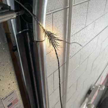 Frayed steel cable near a garage door mechanism inside a workshop.