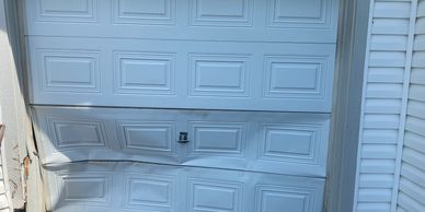 Damaged white garage door with dents and creases.