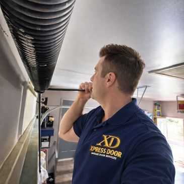 Technician inspecting and repairing a garage door spring inside a garage.