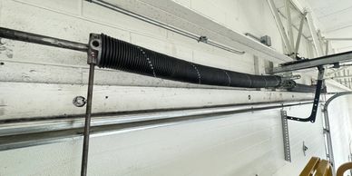 Close-up of a garage door torsion spring system mounted on a white wall.