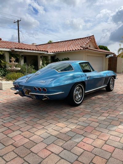 Classic blue Corvette parked on a brick driveway in front of a house.
