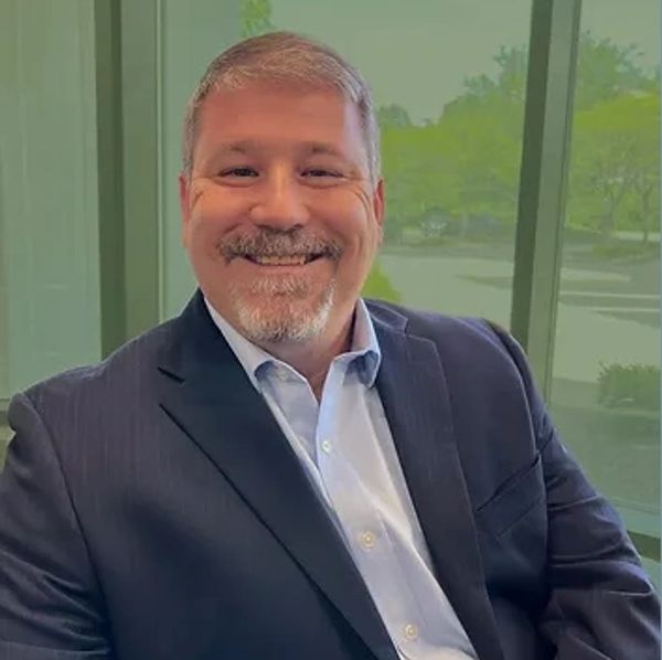 Photo of Bobby Handley, in a suit jacket and collared shirt, with a green background. 