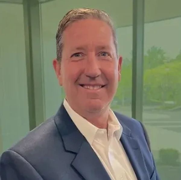 Photo of Robert Ochall, in a suit jacket and collared shirt, with a green background. 