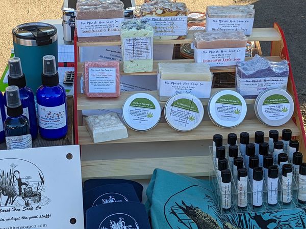 Display of handmade soaps, balms, sprays, and clothing at a market stall.
