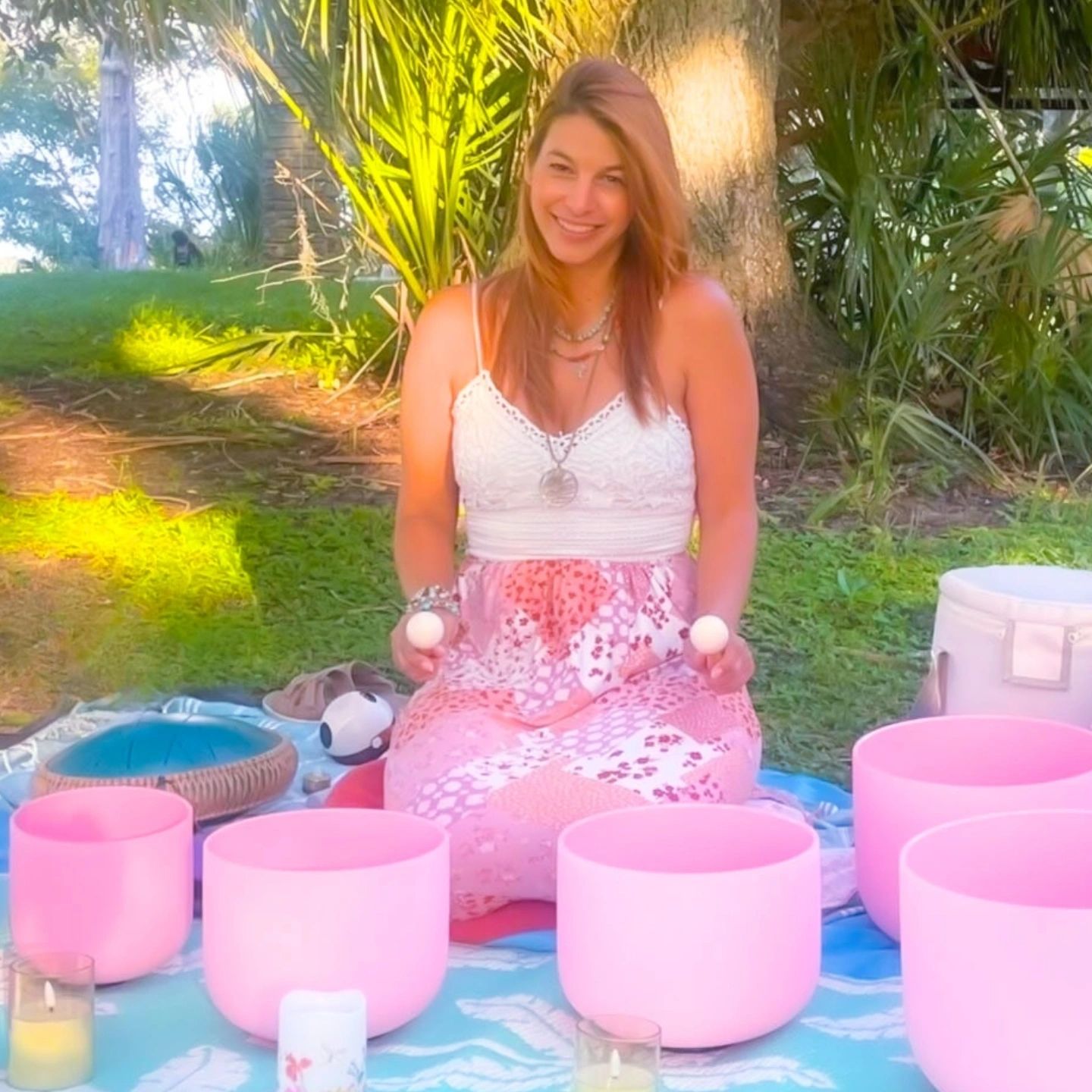 Woman smiling while playing pink crystal singing bowls outdoors.