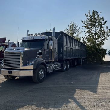 A large black semi-truck parked on a gravel lot near trees.