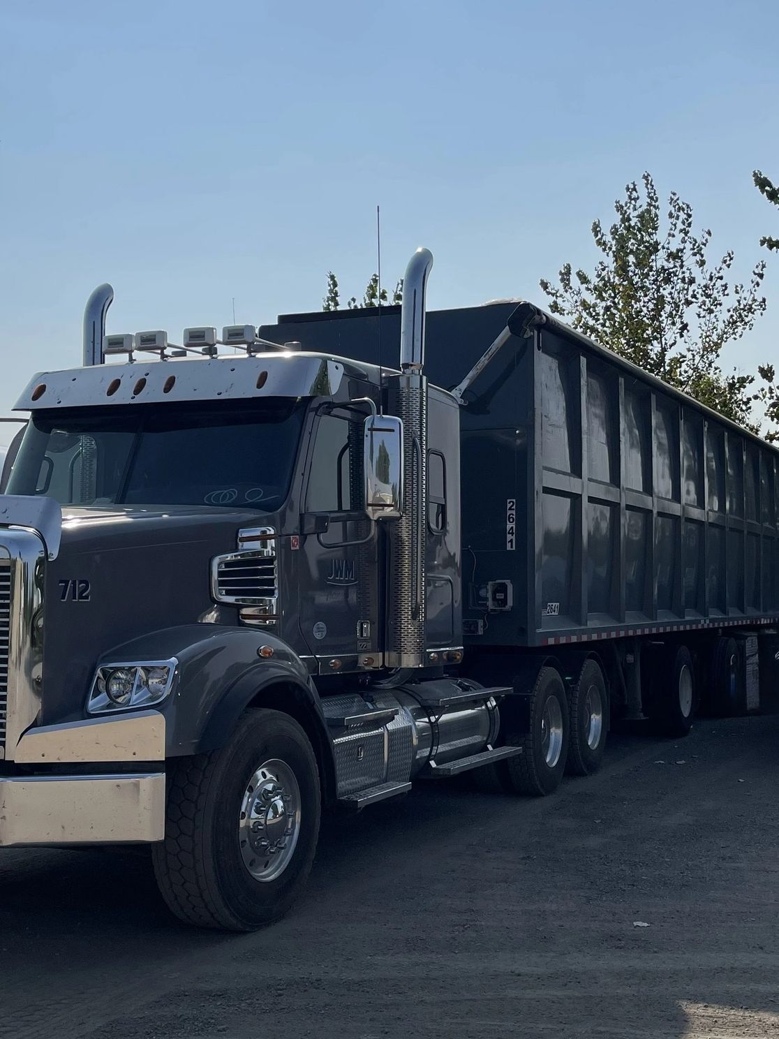 A large gray semi-truck with a trailer parked on a dirt road.