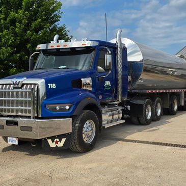Blue Western Star tanker truck parked on a dirt road under a partly cloudy sky.
