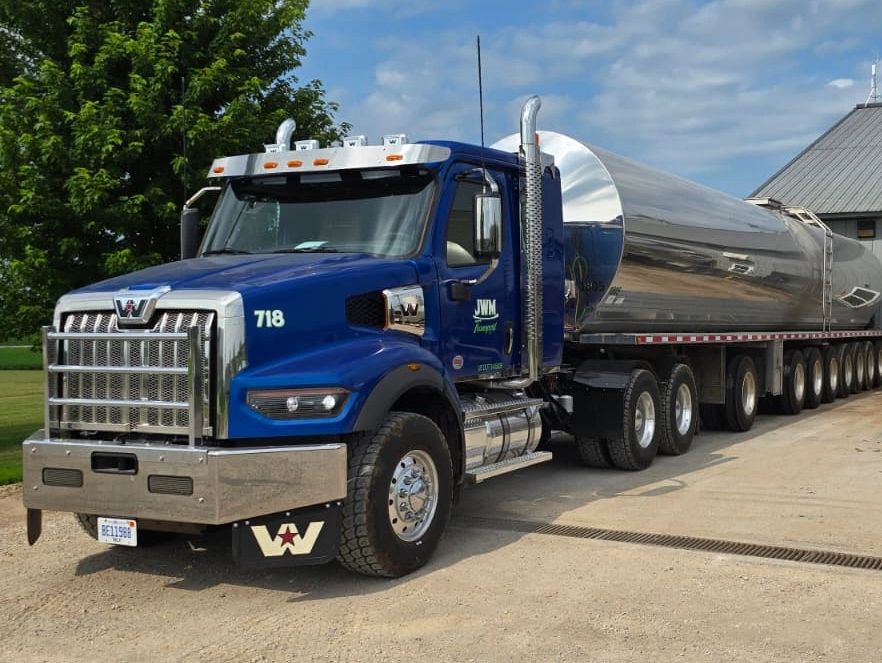 Blue Western Star tanker truck parked on a dirt road near a building.