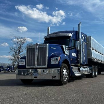 Blue Kenworth semi-truck parked on asphalt under a partly cloudy sky.