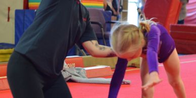 Girl learning gymnastics with coach's support.