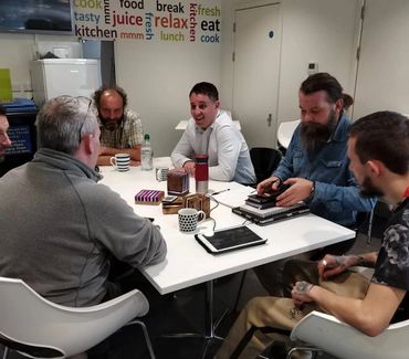 A group of six men having a meeting around a white table.