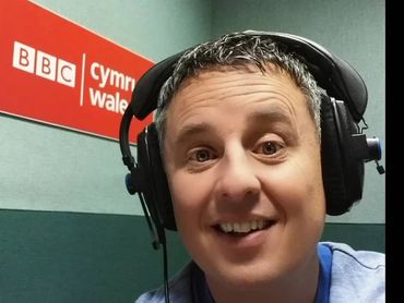 Man with headphones in BBC Cymru Wales studio, smiling for a selfie.