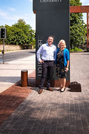 Two people standing in front of Oxford Brookes University sign, smiling.