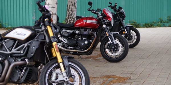 Three motorcycles parked in a row on a paved area near trees.