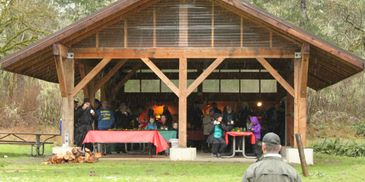 People gathered under a wooden pavilion in a park.