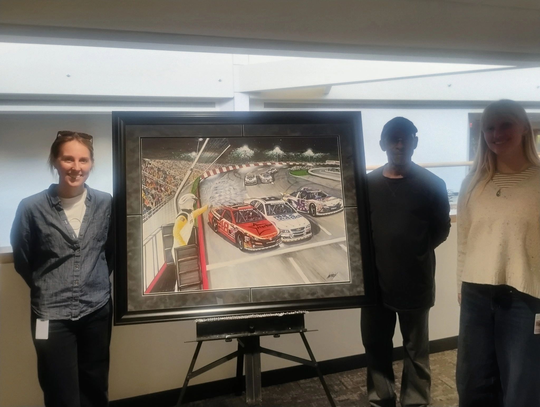 Three people stand on either side of a racing-themed painting.