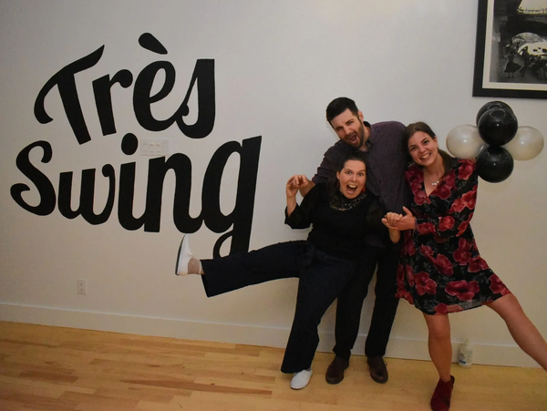 Les trois associés de l'école Très Swing, prenant une pose festive devant leur logo peint au mur.