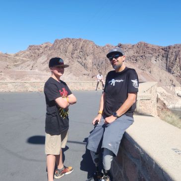 Two men posing near rocky terrain on a sunny day.