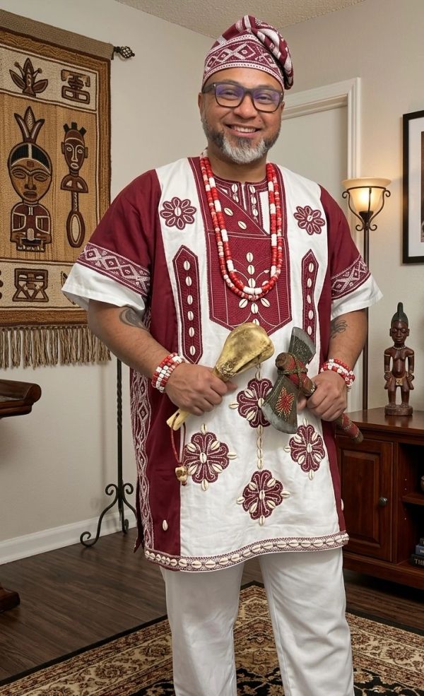 Man dressed in traditional African attire holding ceremonial objects.