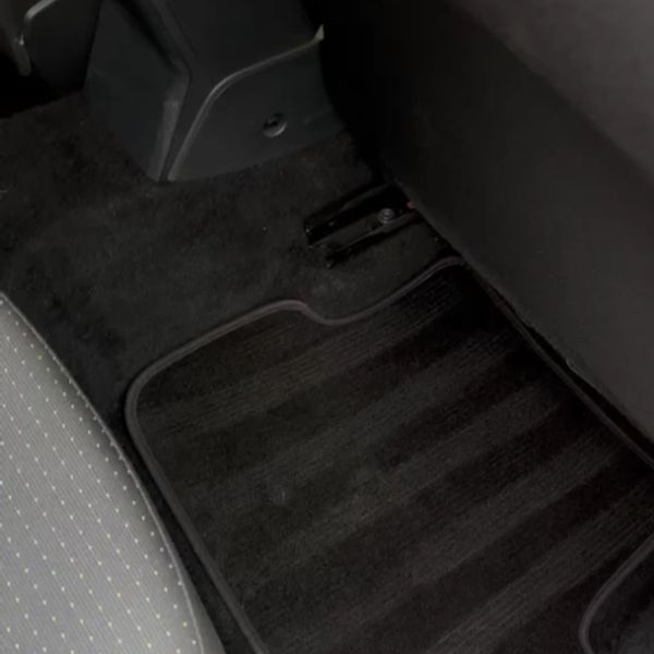 Clean black car floor mat and carpeted area beside a gray fabric car seat.