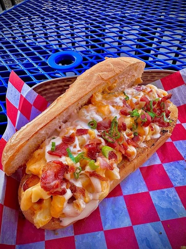Mac and cheese on a toasted hoagie topped with bacon and chives in a dish sat on a blue picnic table