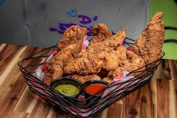 breaded chicken tenders in a basket with various sauces in a black basket dish