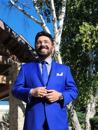 Man in a bright blue suit smiling outdoors on a sunny day.