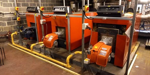 Industrial orange boilers with yellow piping in a Plant room.