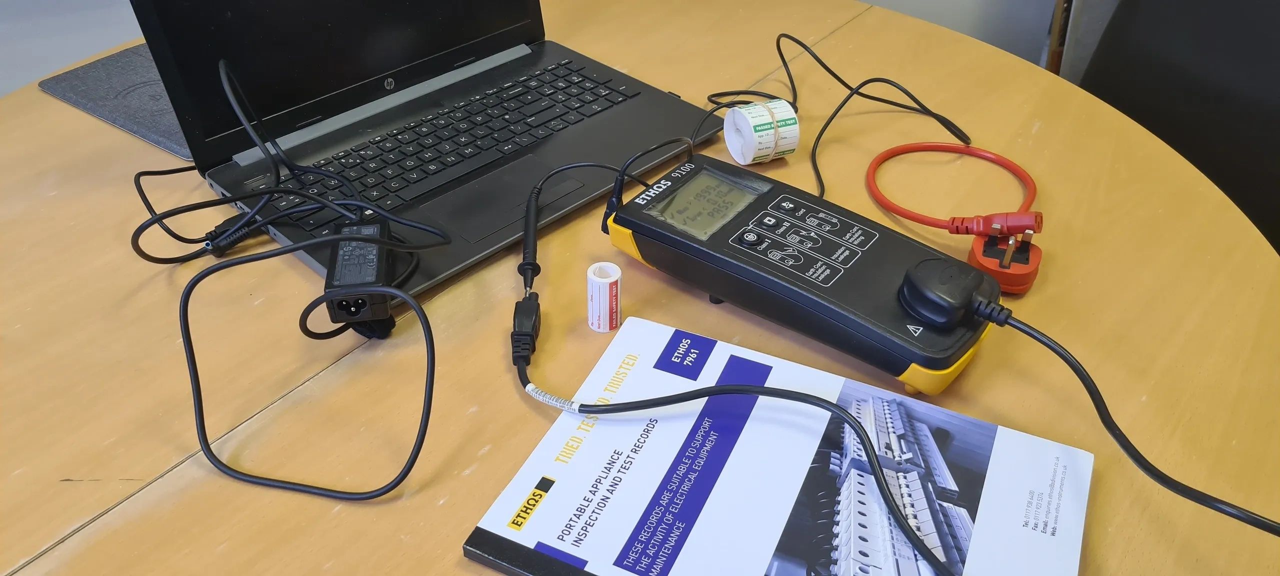 Electrical testing equipment and laptop on a wooden table.