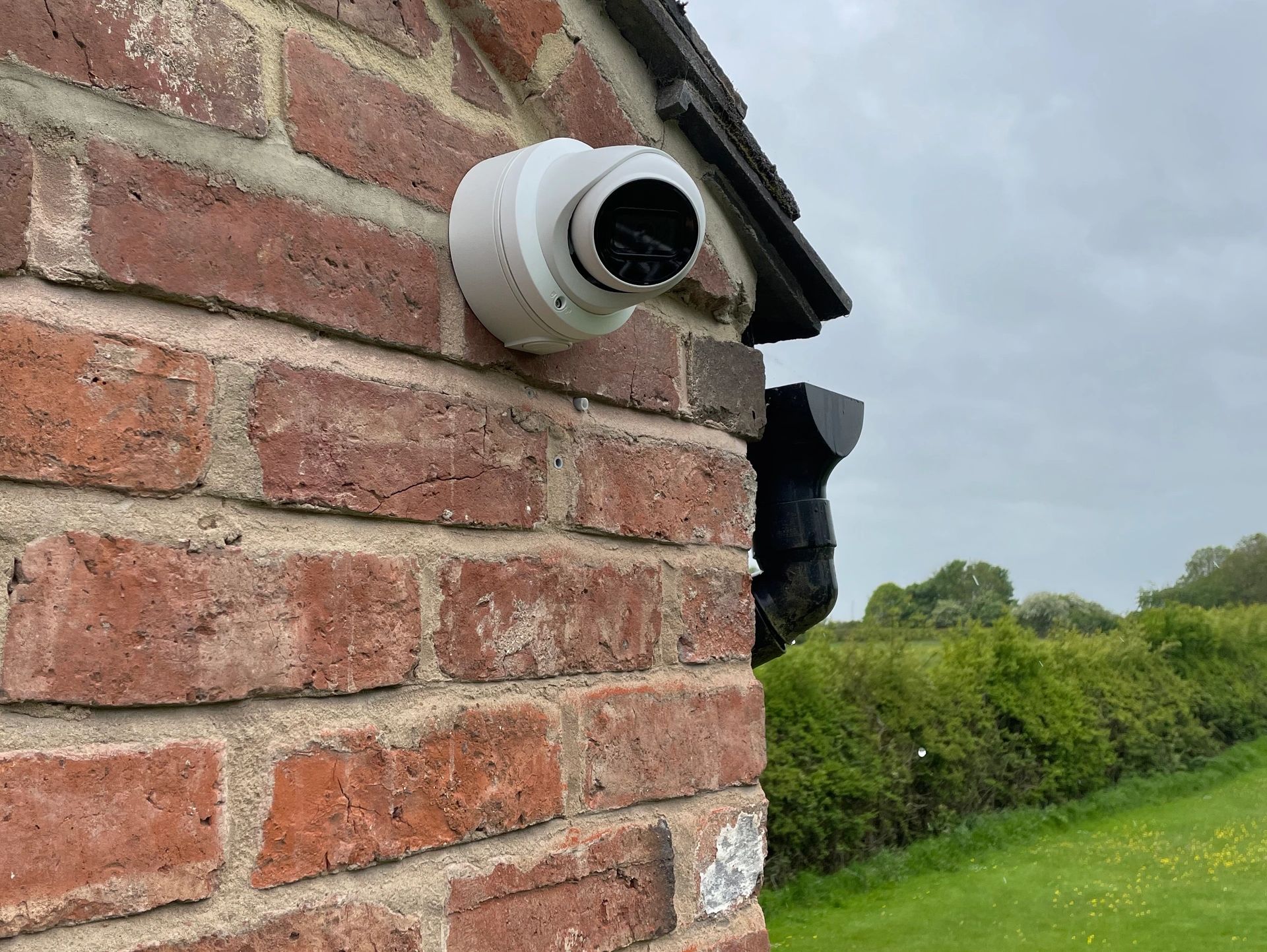 Security camera mounted on a red brick wall outside.