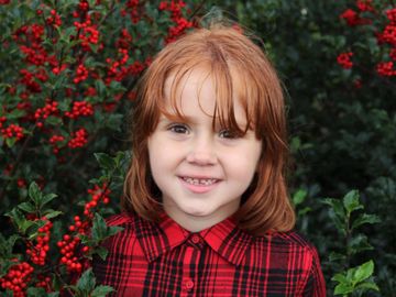 A photo of a little girl with red hair, a red plaid shirt and a berry bush with a nice smile 